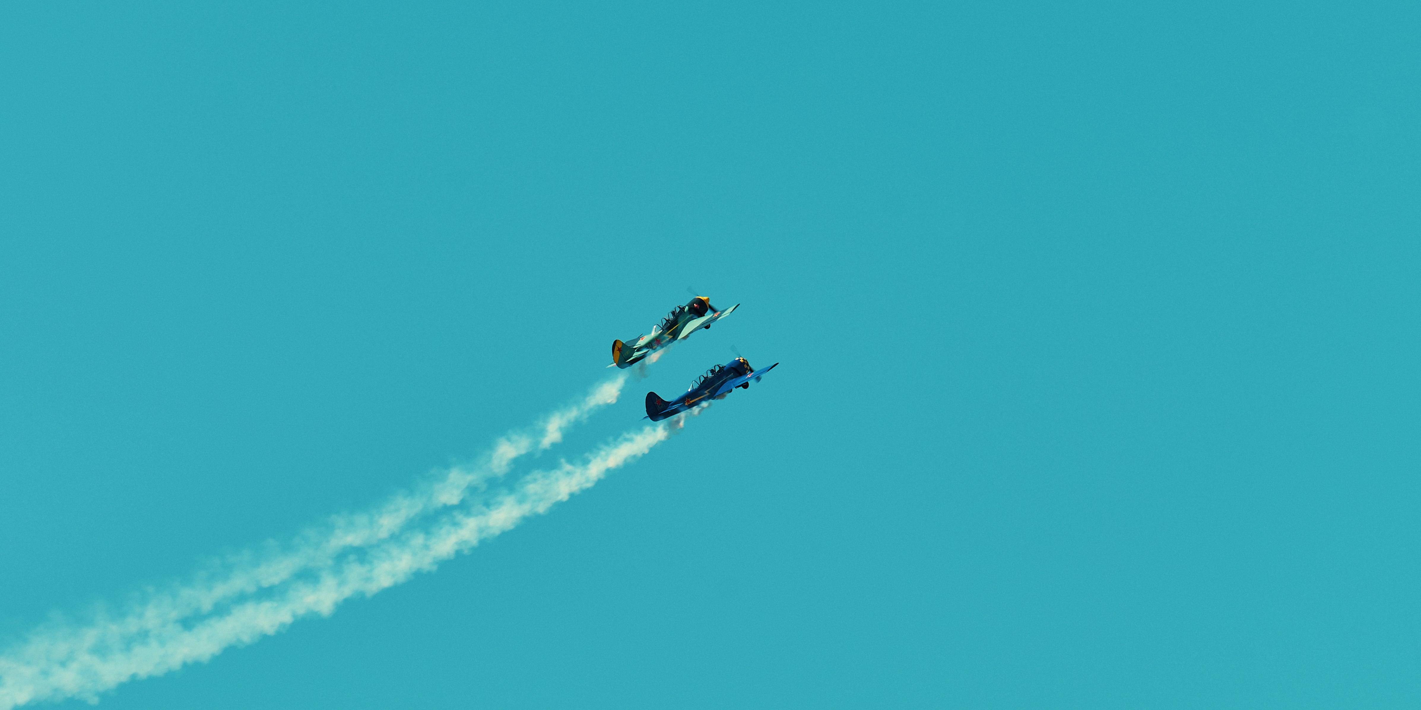 two blue planes in blue sky leaving white smoke trails